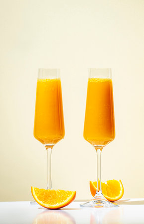 Mimosa alcohol cocktail drink with orange juice and cold dry champagne or sparkling wine in glasses. Beige background, hard light, shadow patternの写真素材