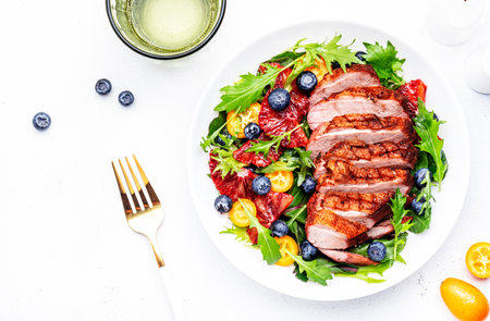 Duck slices salad with grilled breast and bloody orange, kumquat, blueberry and chard, frisse, mizuna, arugula leaves on white table background, top viewの写真素材