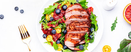 Duck slices salad with grilled breast and bloody orange, kumquat, blueberry and chard, frisse, mizuna, arugula leaves on white table background, top view bannerの写真素材