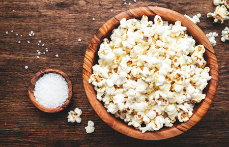 Salted popcorn in wooden bowl, unhealthy food, wooden kitchen table background, top viewの写真素材