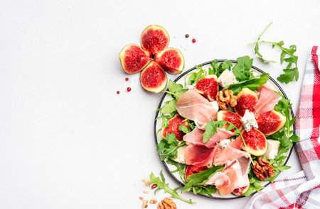 Summer salad with sweet figs, prosciutto, gorgonzola cheese, walnuts, arugula on white kitchen table background, top view, copy spaceの写真素材