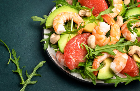 Healthy fresh salad with shrimps, avocado, grapefruit, arugula and cashews. Dark green kitchen table background, top view, close-upの写真素材
