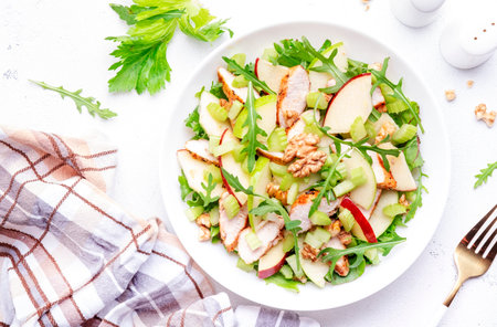 Waldorf salad with red and green apple, celery, lettuce, chicken fillet, arugula and walnuts on plate, white table background, top viewの写真素材