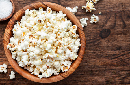 Salted popcorn in wooden bowl, unhealthy food, wooden kitchen table background, top viewの写真素材