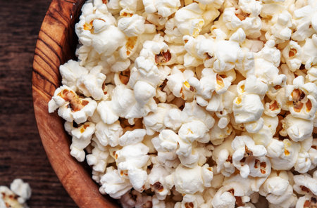 Salted popcorn in wooden bowl, unhealthy food, wooden kitchen table background, top viewの写真素材