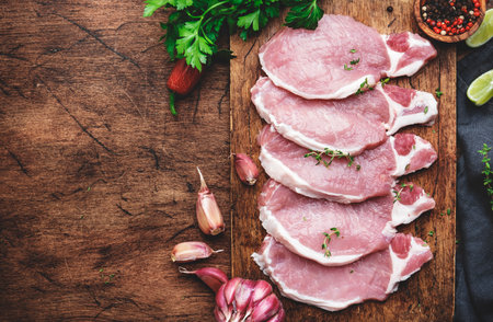 Raw pork chops on rustic wooden cutting board prepared for cooking with garlic, thyme, spices and pepper. Old wood kitchen table, top viewの写真素材