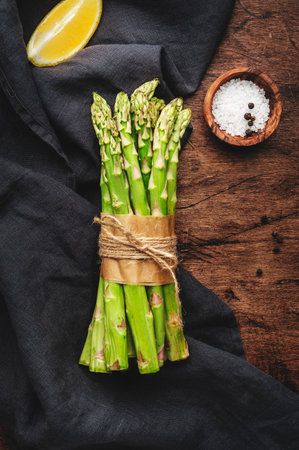 Fresh asparagus bunch, lemon and sea salt on rustic wooden kitchen table background, top view, copy spaceの写真素材