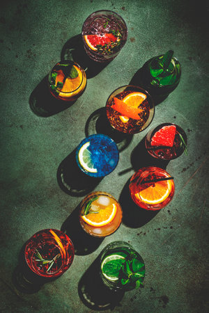 Cocktails set on rusty green bar counter, top view. Mixology concept. Assortment of colorful strong and low alcohol drinks for summer cocktail party. Dark background, hard lightの写真素材