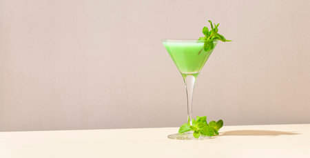 Grasshopper green alcoholic cocktail drink with mint liqueur, cream, ice and fresh mint. Beige background, hard light, shadow pattern, copy spaceの写真素材