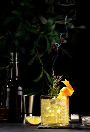 Penicillin cocktail drink with scotch, whiskey, syrup, lemon juice and ice in glass with orange zest, garnished with steaming rosemary. black backgroundの写真素材