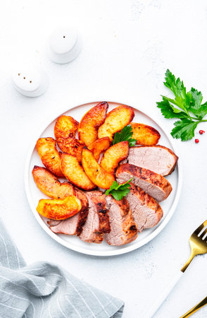 Baked pork tenderloin and quince or apple slices with parsley served on white plate. White table background, top viewの写真素材