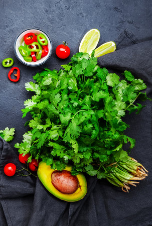 Fresh cilantro or coriander, chili and jalapeno peppers, avocado, lime and cherry tomatoes - ingredients for Mexican spicy cuisine. Black kitchen table background, top viewの写真素材