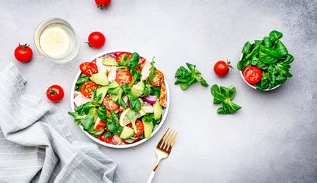 Chicken and vegetables salad with tomatoes, avocado, cucumber, onion, lamb lettuce and sesame seeds on gray table background, top viewの写真素材