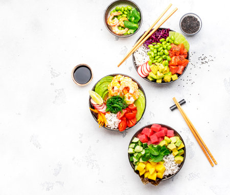 Poke bowl set: tuna, salmon, shrimps with avocado, fruits and vegetables, white rice and other ingredients. Hawaiian food dish. White table background, top viewの写真素材