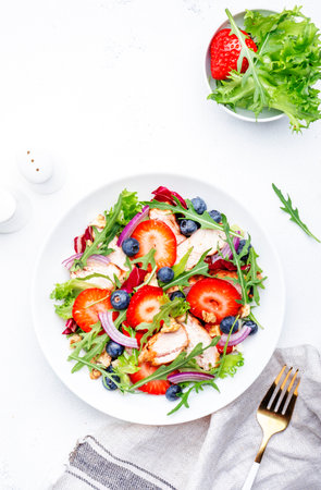 Summer strawberry and grilled chicken healthy salad with arugula, blueberries, red onion and walnuts, white table. Fresh useful dish for eating healthyの写真素材