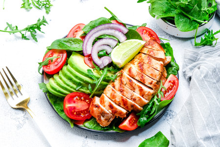 Healthy vegetable salad with grilled chicken fillet, spinach, tomatoes, avocado and onion with olive oil on white table background. Tasty detox, ketogenic diet food. top viewの写真素材