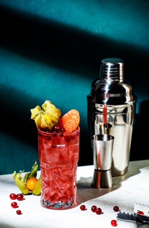 Sea breeze alcoholic cocktail drink with vodka, cranberries, grapefruit juice, orange and ice with physalis. bar tools. Dark green background, hard light, shadow patternの写真素材