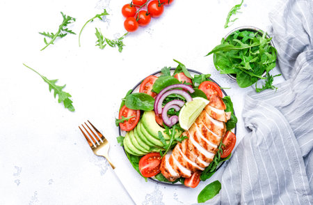 Healthy vegetable salad with grilled chicken fillet, spinach, tomatoes, avocado and onion with olive oil on white table background. Tasty detox, ketogenic diet food. top viewの写真素材