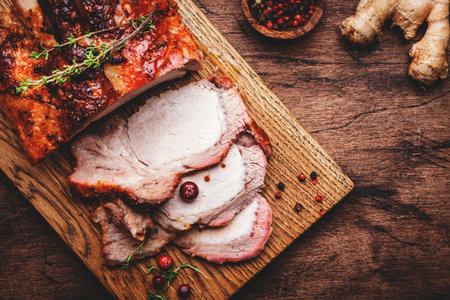 Baked pork loin on rustic wooden cutting board with spices, herbs and cranberries. Wood kitchen table background, top viewの写真素材
