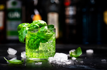 Basil smash alcoholic cocktail drink with dry gin, syrup, lemon, basil and ice, dark bar counter backgroundの写真素材