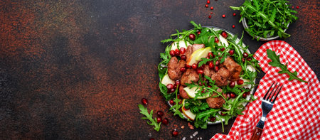 Tasty salad with pan-fried chicken liver, green apple, pomegranate and fresh arugula. Brown table background, top viewの写真素材