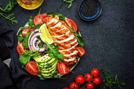 Healthy useful salad with grilled chicken, spinach, tomatoes, avocado and onion with olive oil on black table background. Tasty detox, ketogenic diet food. top viewの写真素材