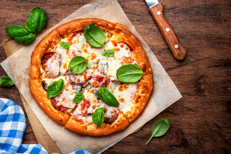 Pizza with spicy salami sausage, mozzarella cheese, tomato sauce and green basil on rustic wooden kitchen table background, top viewの写真素材