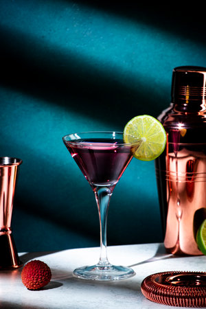 Alcoholic cocktail drink with vodka, dry gin, lychee, lime and ice in martini glass, dark green background, bright hard light and shadow patternの写真素材