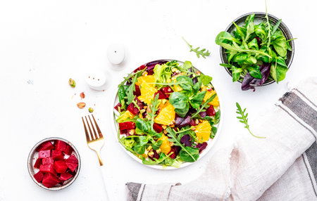 Beetroot and orange salad with arugula, lamb lettuce, mini chard and pistachios, white table, copy space.. Fresh useful dish for healthy eatingの写真素材