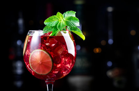 Royal lemonade alcoholic cocktail drink with tequila, dry gin, white rum, vodka, liquor, lime, raspberries and ice in wine glass. Black bar counter background, bar tools and bottlesの写真素材