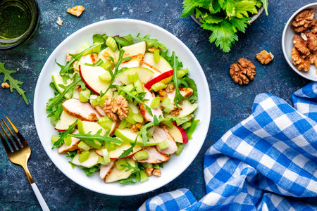 Waldorf salad with fresh apple, celery, lettuce, grilled chicken fillet, arugula and walnuts on plate, blue table background, top viewの写真素材