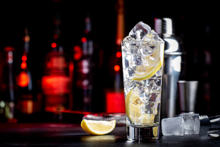 Vodka tonic alcoholic cocktail drink with cold vodka, lemon juice, bitter tonic and ice cubes. Black background, bar counter with bottlesの写真素材