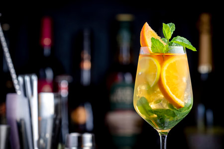 White sangria summer alcoholic drink with white spanish wine, peach, orange, lime and ice. Black bar counter background, steel bar tools and bottlesの写真素材