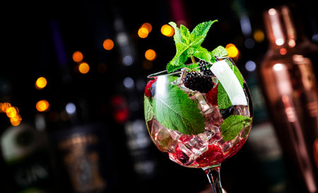 Mojito sangria alcoholic cocktail drink with white rum, prosecco or sparkling wine, lime juice, raspberry, blueberry, blackberry and ice in wine glass, dark bar counter background, bar tools and bottlesの写真素材