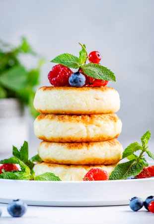 Thick pancakes with cottage cheese with blueberries, raspberries and red currants, decorated with mint on white plate, delicious breakfast. gray table backgroundの写真素材