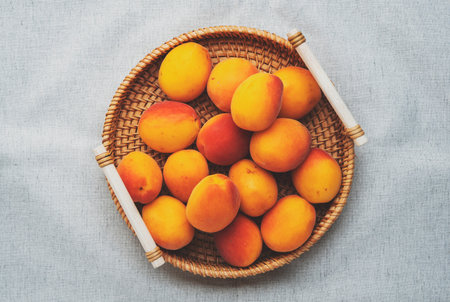 Fresh red orange apricots in wicker tray on gray linen background, top viewの写真素材