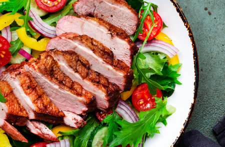 Salad with grilled duck breast slices and cherry tomatoes, cucumber, paprika, red onion, lettuce and arugula on green table background, top viewの写真素材