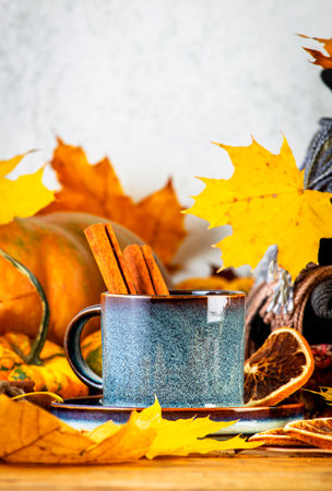 Autumn drink in blue cup on fall background with pumpkins, orange fallen leaves, autumn clothes, scarves on rustic wooden table, copy spaceの写真素材