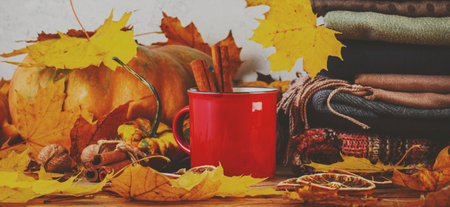 Autumn drink in red cup on fall background with pumpkins, orange fallen leaves, autumn clothes, scarves on rustic wooden table, copy space, bannerの写真素材