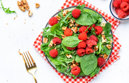 Delicious vegan salad with raspberries, red onion, walnuts, spinach and mixed greens, white table...