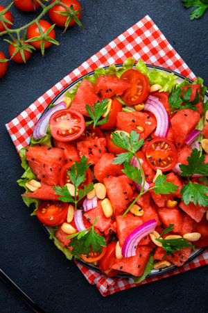 Gourmet salad with sweet juicy watermelon, cherry tomatoes, red onion, peanuts and parsley, black table background, top viewの写真素材