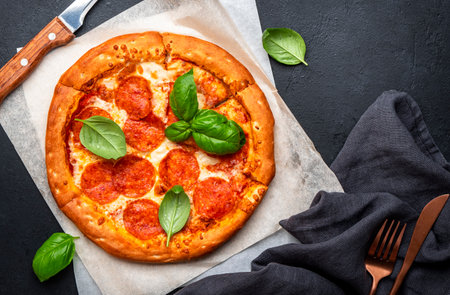 Hot Pepperoni pizza with salami sausage, cheese, spicy tomato sauce and green basil leaves, ready to eat, black background, top viewの写真素材
