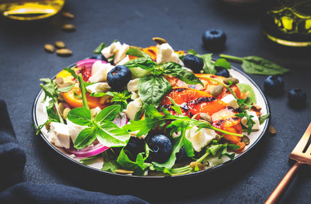 Gourmet salad with grilled peaches, blueberries, red onion, feta cheese, basil and mixed herbs, black table background, top viewの写真素材