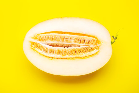 Large oval melon, cut half with seeds on bright yellow background, top viewの写真素材
