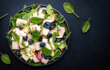 Gourmet salad with juicy sweet melon, grilled chicken, red onion, cheese, blueberries and mixed herbs, black table background, top viewの写真素材