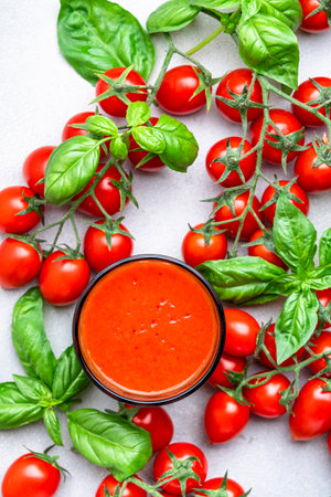 Freshly squeezed tomato juice glass and red cherry tomatoes with green basil leaves on gray table background, top viewの写真素材
