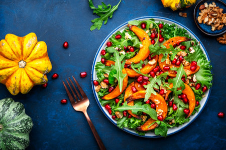 Vegan autumn salad with baked sweet pumpkin, lettuce, arugula, pomegranate seeds and walnuts. Comfort slow food. Blue background. Top viewの写真素材