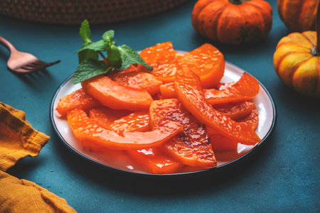 Baked pumpkin slices caramelized in orange glaze, autumn or winter dessert food on dark green table background. Top viewの写真素材