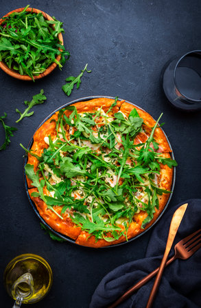 Hot homemade pizza with blue cheese, ham, pesto sauce and fresh arugula, black table background, top viewの写真素材