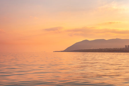 Sea panorama at sunset, silhouettes of the coast and mountains against the background of the pink orange setting sunの写真素材